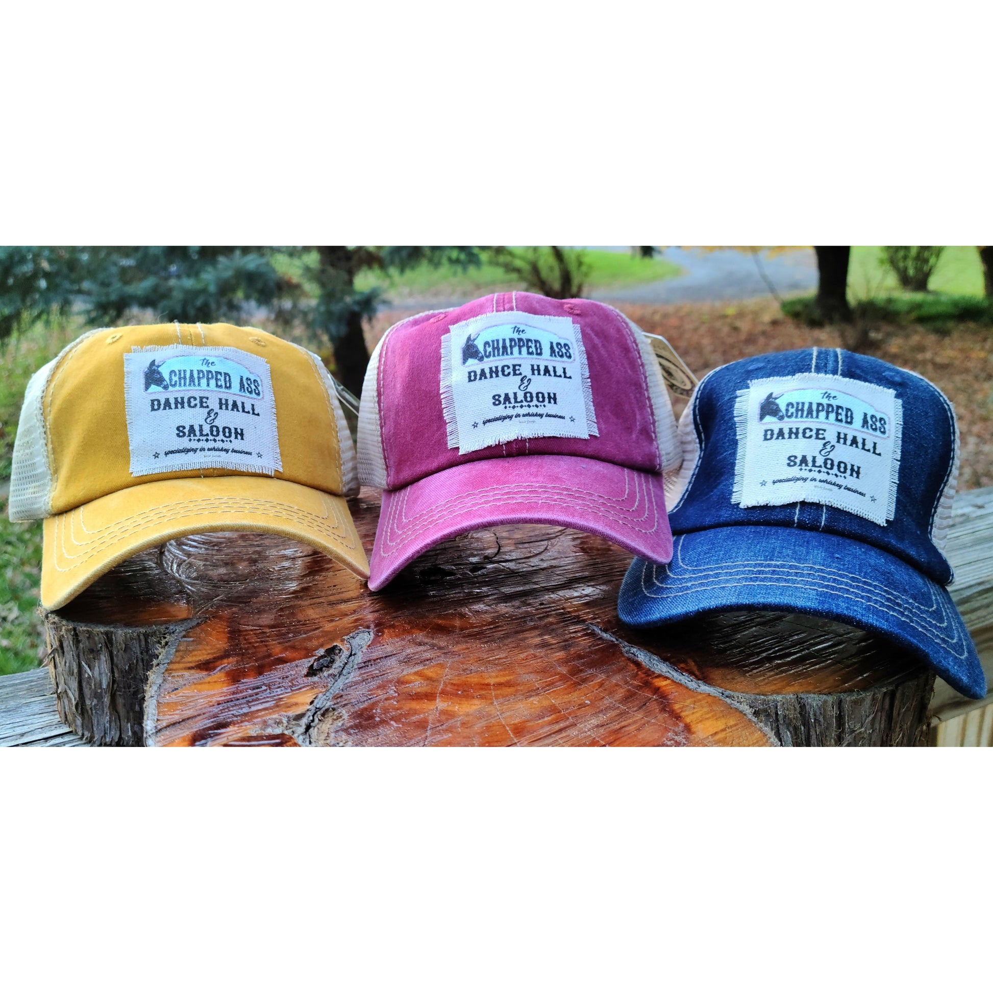 Three Trucker hats featuring the chapped ass dance hall and saloon with a donkey on it. Comes in Yellow, Red, or Blue